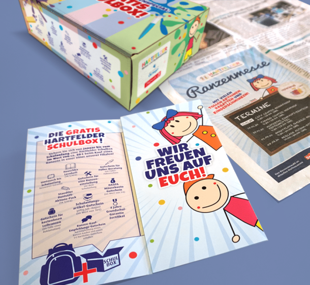 Diverse Werbemittel für die Ranzenmessen von Hartfelder Marken- und Qualitätsspielzeug bestehend aus einem Flyer, einer Box mit verschiedenen Schulmaterialien sowie einer Zeitungsanzeige